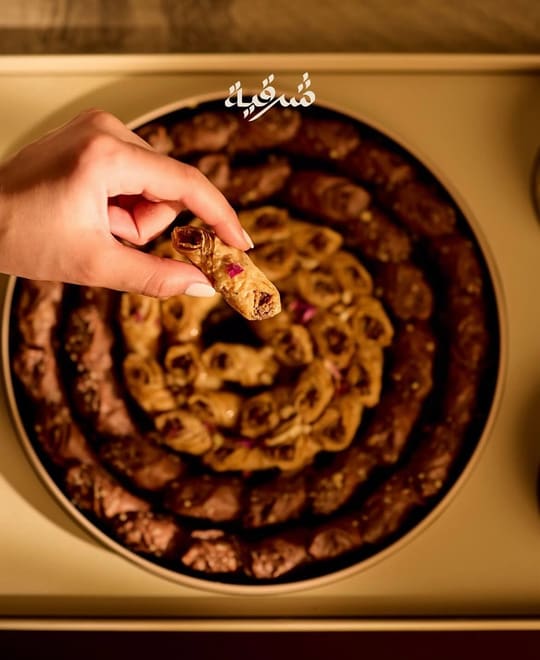 يد تلتقط قطعة من صينية حلويات شرقية دائرية